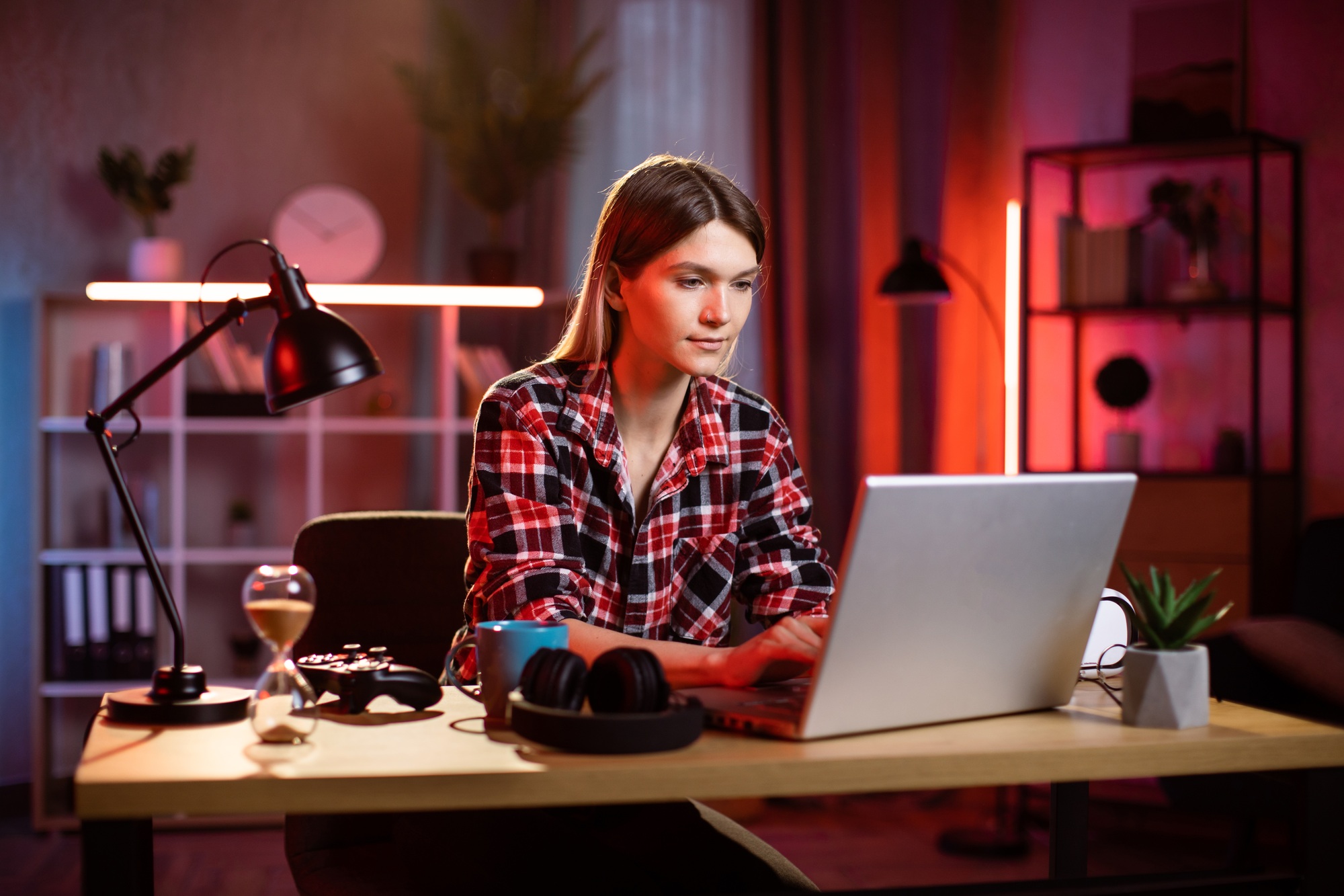 Beautiful young woman in checkered shirt sitting at home office and typing on wireless laptop.